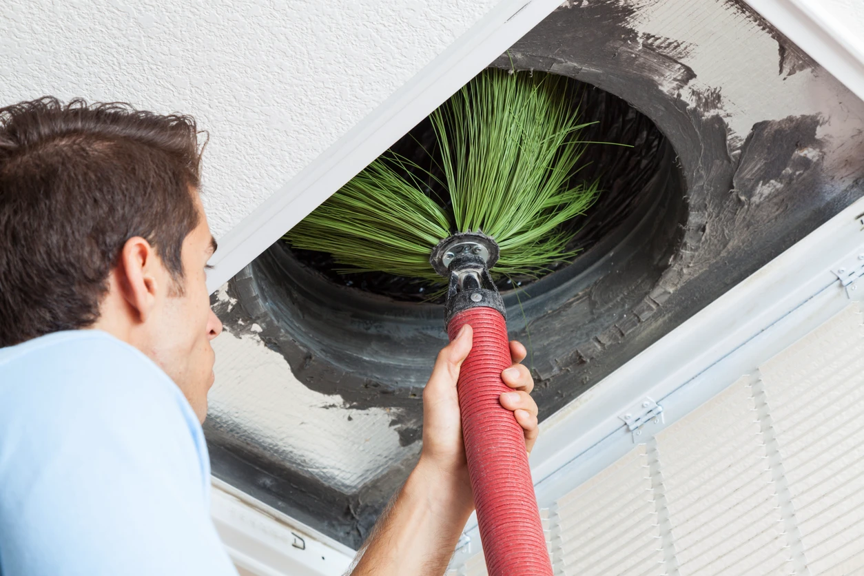 A man using a green brush to clean a duct