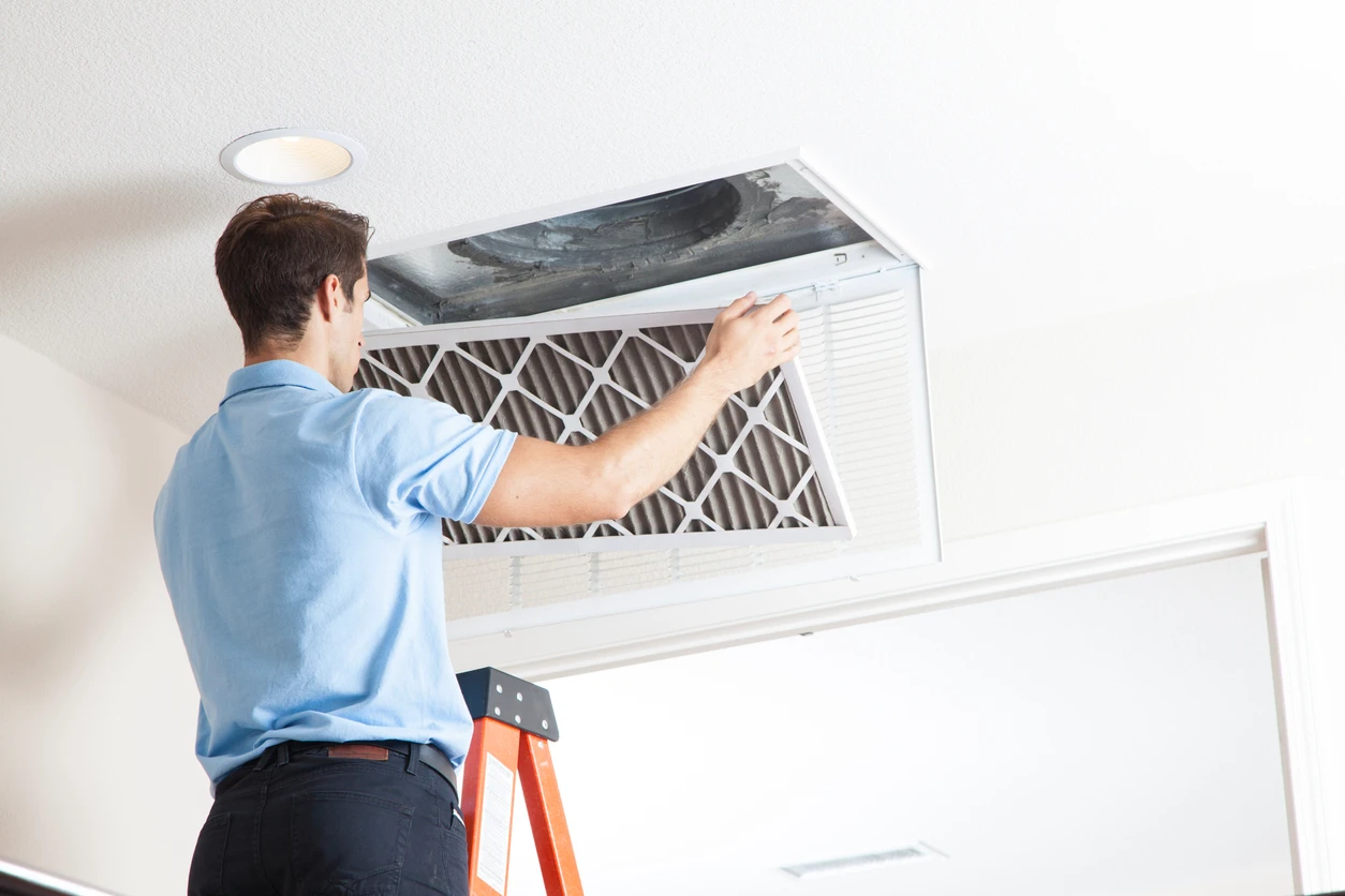 A man installs an air filter on the ceiling